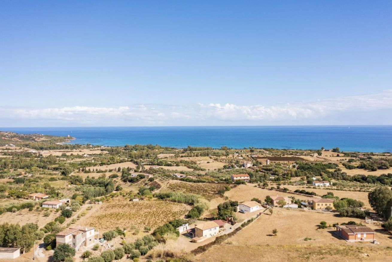 An aerial view of a coastal village with houses, fields, and the sea in the background.