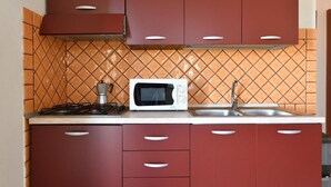 A kitchen with red cabinets, a microwave, and a gas stove. - Residence Sole - Apartment 1 (Tertenia)