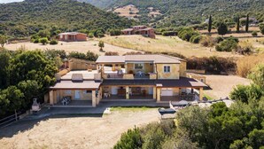 A large, two-story house with a patio and outdoor seating area, surrounded by a hilly landscape. - Residence Sole - Apartment 1 (Tertenia)