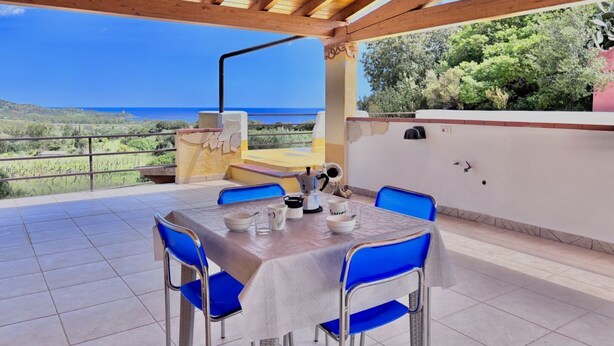 A covered outdoor dining area with a table set for four, chairs, and a view of the sea. - Residence Sole - Apartment 2 (Tertenia)