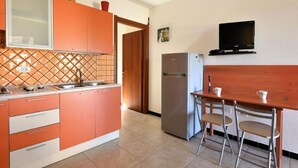 Une cuisine compacte avec des meubles de couleur orange, un réfrigérateur en acier inoxydable et une petite table à manger avec deux chaises.