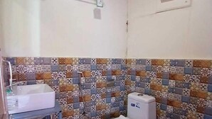 Et lille badeværelse med toilet, et vaskeskrin, et håndklædestativ og en flisebeklædt bagvæg med mønster.