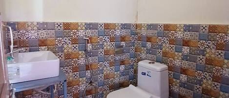 Uma casa de banho pequena com sanita, lavatório apoiado, porta-toalhas e painel de azulejos estampados.