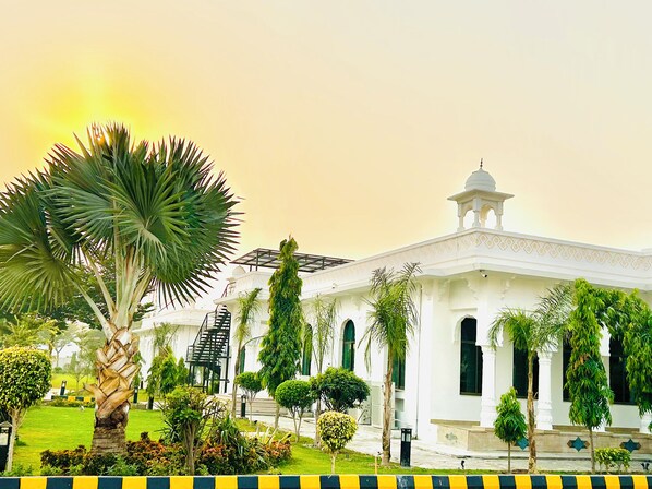 A white building with a dome and arched windows, surrounded by palm trees and well-maintained lawns.