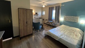 Une chambre d’hôtel de taille réduite comprenant un lit, un bureau avec une chaise, une kitchenette et une armoire.