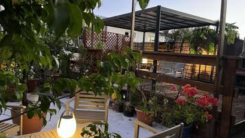 Ein Patio im Freien mit Holzmöbeln, Topfpflanzen und einer überdachten Sitzgelegenheit.