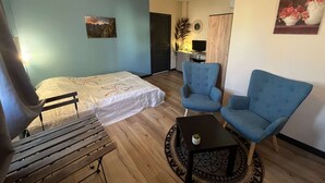Une chambre à coucher avec un lit, deux fauteuils bleus, une petite table et un bureau avec un ordinateur.