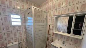 Une salle de bain comprenant des toilettes, une douche fermée par une paroi de verre et un lavabo avec un miroir au-dessus.