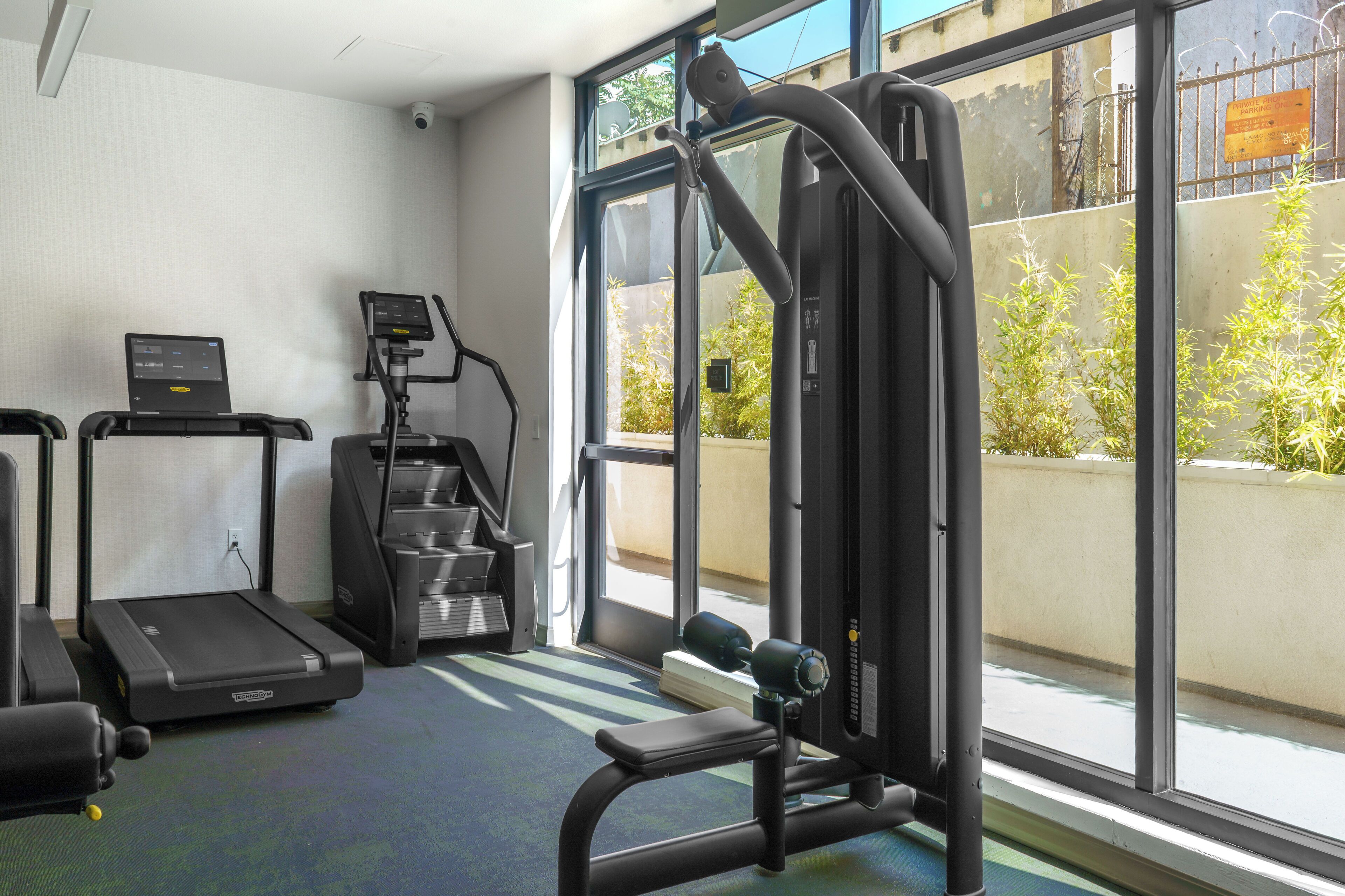 A gym with treadmills, a weight machine, and a window with a view of greenery and a building.