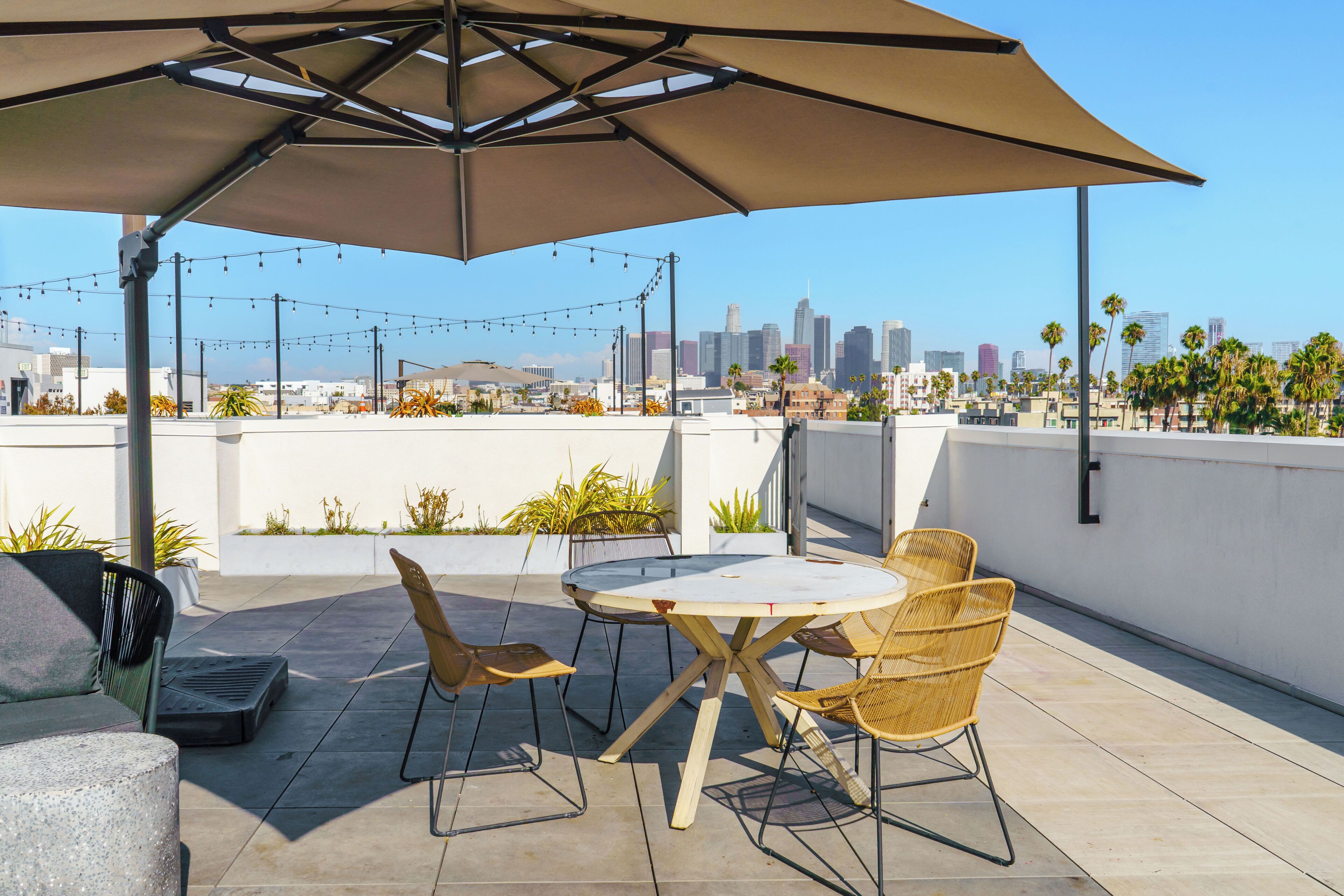 A rooftop patio with a round table and chairs, a large umbrella, and a city skyline view.