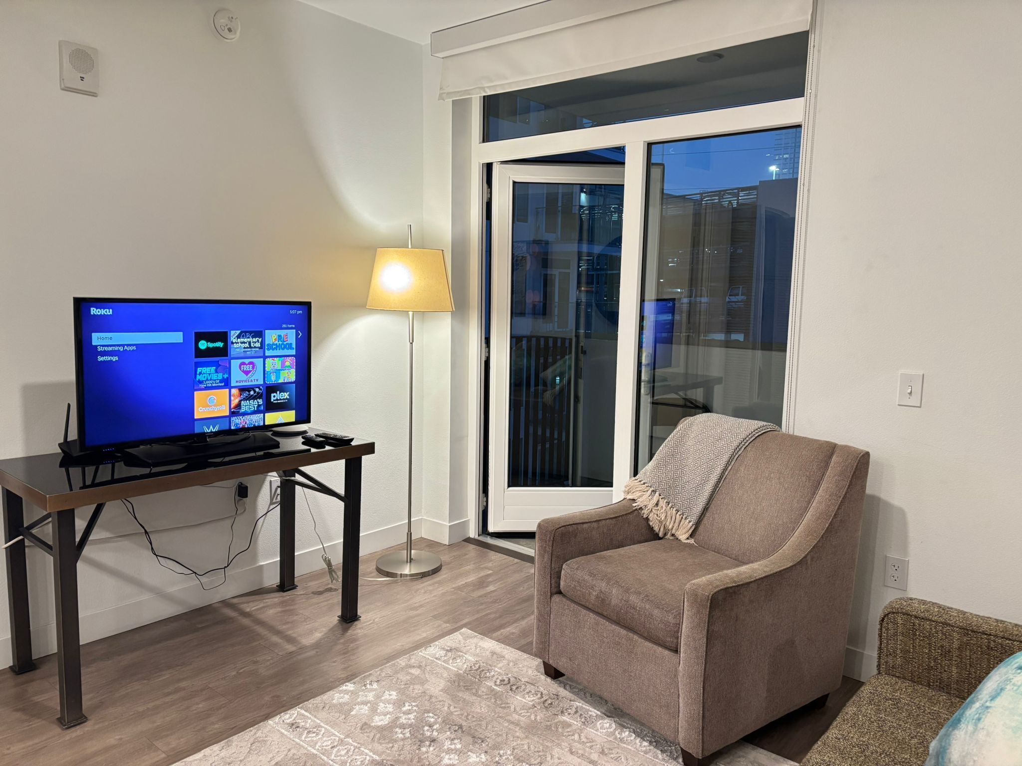 Una sala de estar con un televisor de pantalla plana, una lámpara, un sofá y un tapete estampado.
