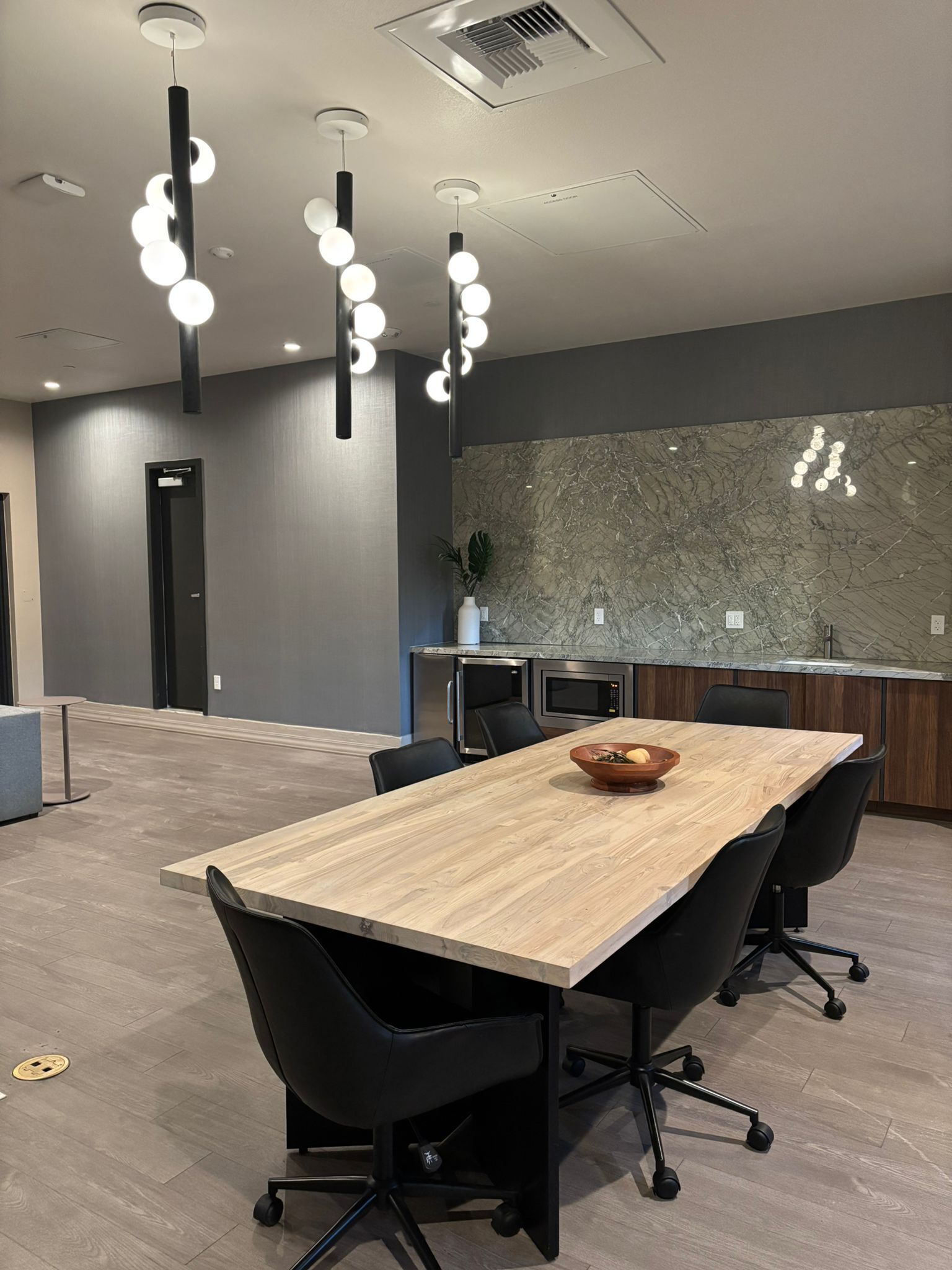 A modern conference room with a wooden table, black chairs, and pendant lighting.