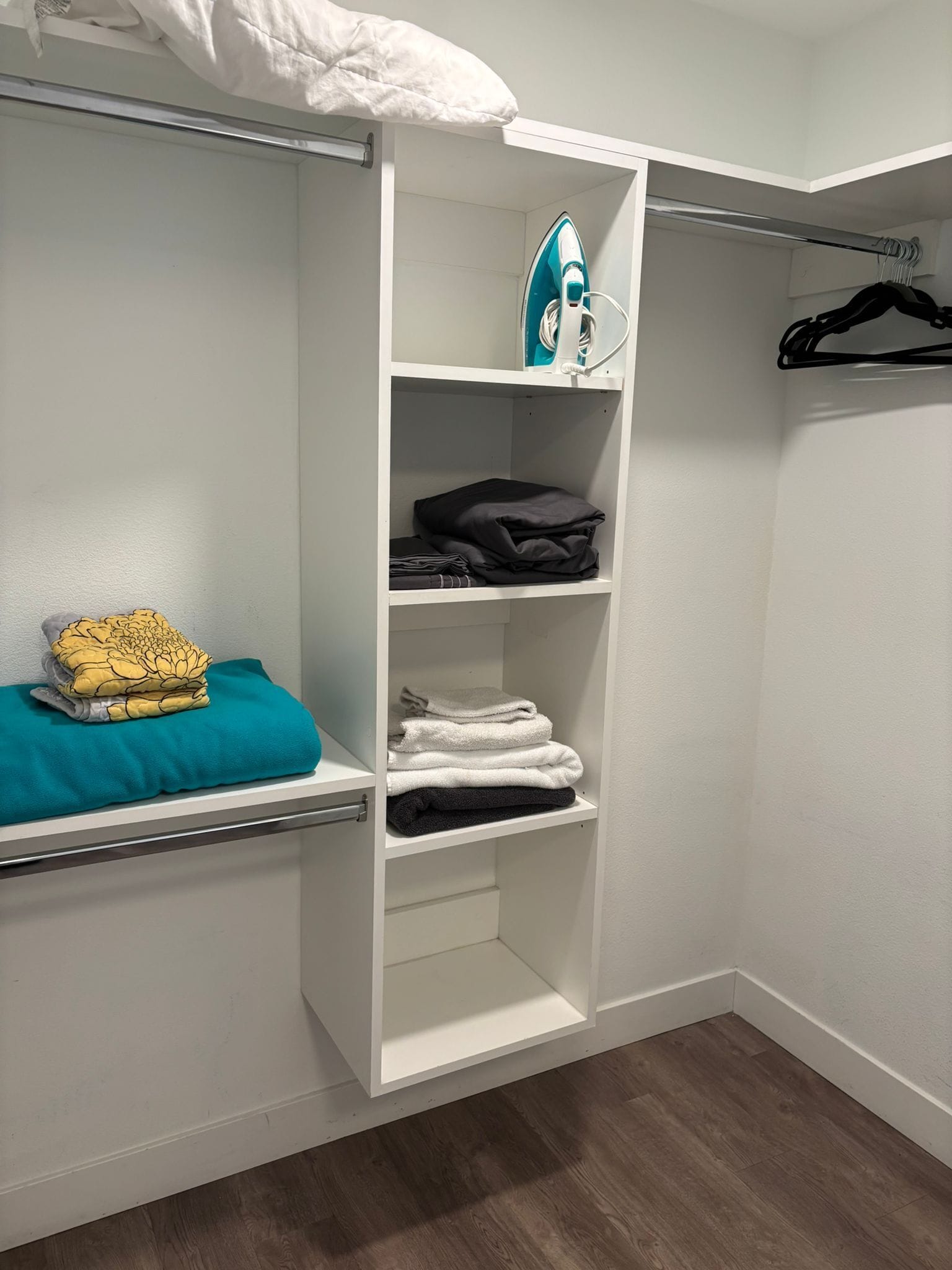 A walk-in closet with white shelving, a hanging rod, and a folded towel on the left.
