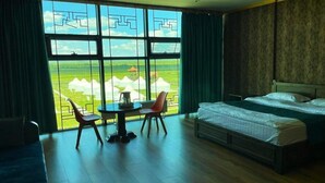 A hotel room with a large window, a bed, a chair, and a small table. - Secret of the Silk Road (Kharkhorin)