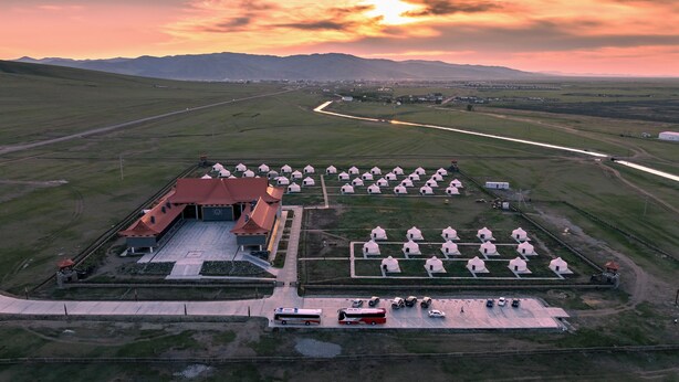 An aerial view of a facility with a central building, a parking area, and multiple yurts arranged in rows. - Secret of the Silk Road (Kharkhorin)