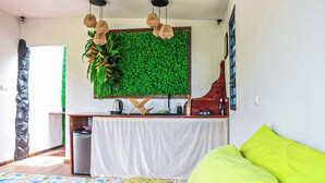 A compact bedroom with a bed, a small kitchenette, and a green wall with a plant.