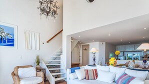 Ein Wohnzimmer mit einem weißen Sofa, einem Korbsessel, einer Treppe und einer Pendelleuchte.