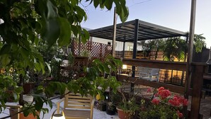 An outdoor patio area with wooden furniture, potted plants, and a covered seating area. - Studio Zoizo White (Saint-Pierre)