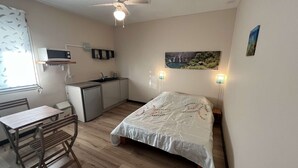 A compact room with a bed, a small kitchenette, a dining table, and a ceiling fan. - Studio Zoizo White (Saint-Pierre)