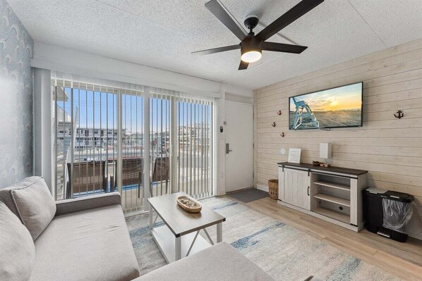 A modern living room with a sofa, a coffee table, a TV, and a ceiling fan.