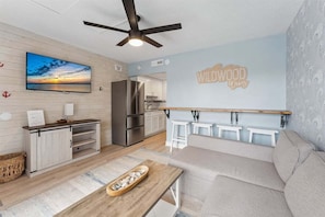 A modern kitchen with a built-in refrigerator, a dining area with a wooden table, and a wall-mounted TV.
