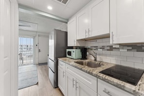 A modern kitchen with white cabinets, a granite countertop, a built-in microwave, a stovetop, and a sink.