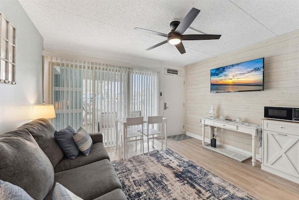 Un salon moderne comprenant un canapé, une table à manger, un téléviseur et un ventilateur de plafond.