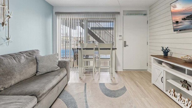 Un salon avec un canapé, une table à manger et des chaises, un téléviseur fixé au mur et un escalier menant à l’étage supérieur.