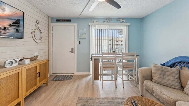A room with a ceiling fan, a dining table with chairs, a sofa, a cabinet, and a wall-mounted TV.