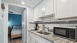 A compact kitchen with white cabinets, a granite countertop, a sink, and a microwave.