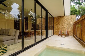 A modern outdoor patio with a stone wall, a glass-enclosed seating area, and a hot tub.