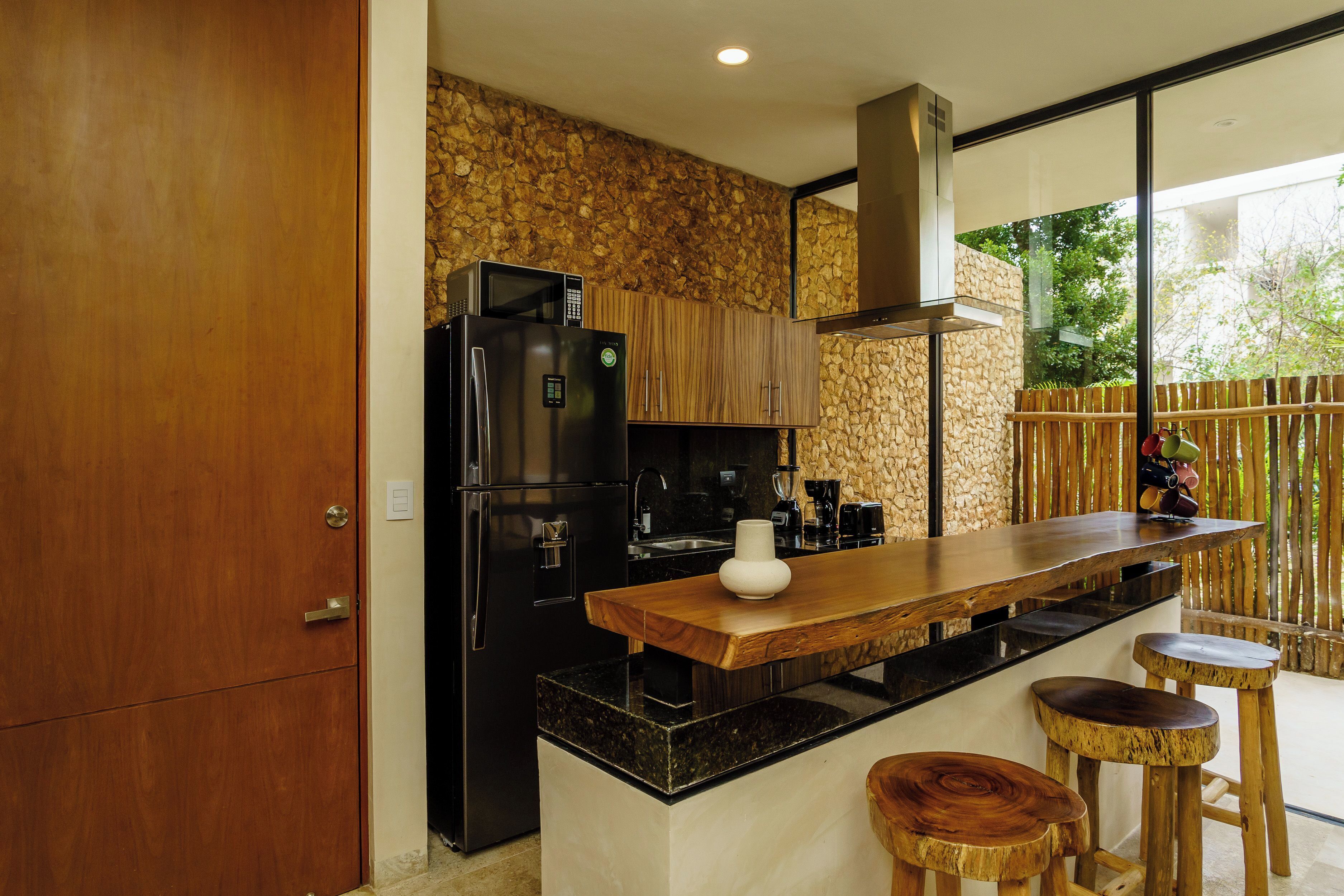 Une cuisine moderne dotée d’un îlot central, d’appareils électroménagers noirs, de meubles en bois et d’un mur d’accent en pierre.