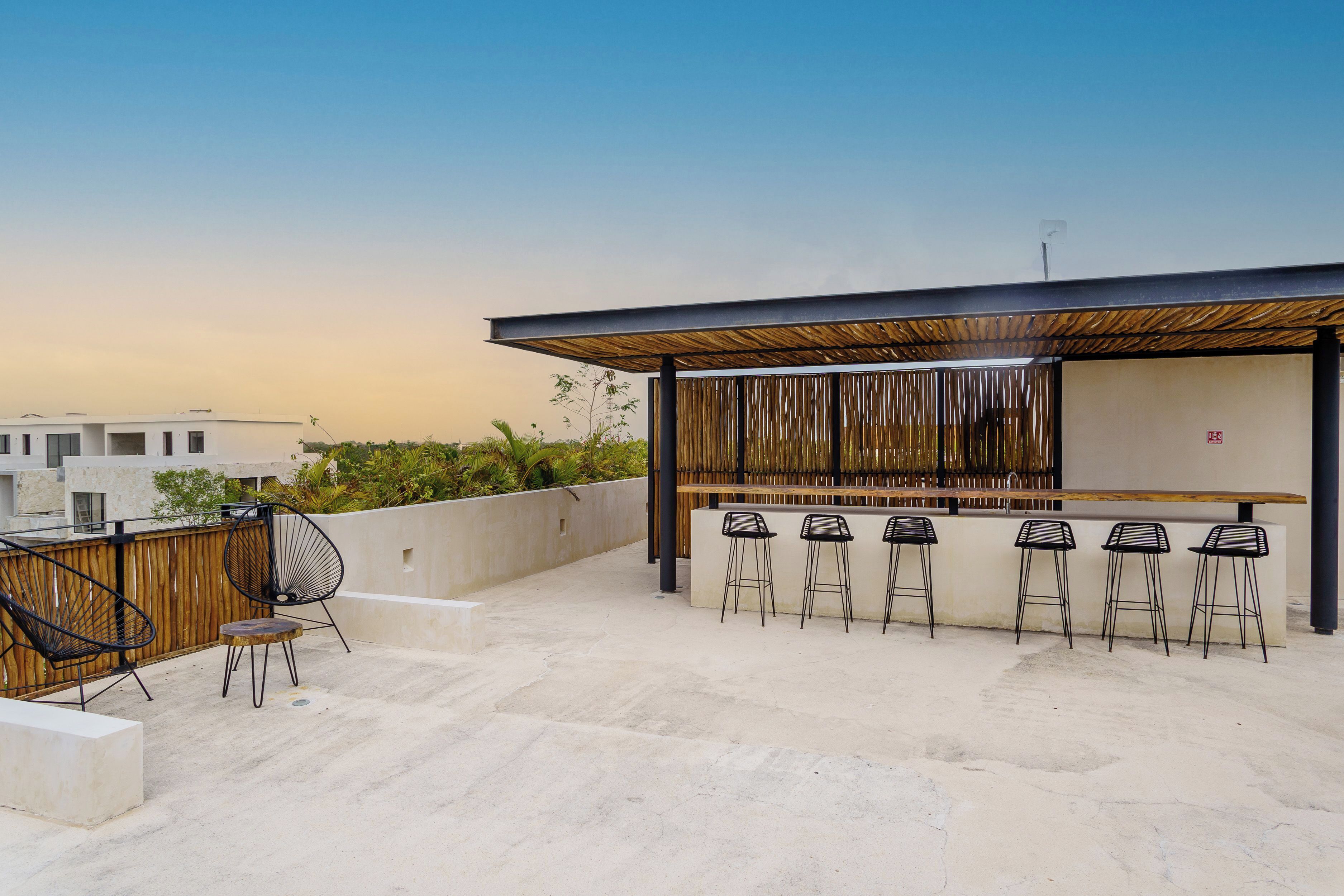 An outdoor bar area with a concrete floor, a wooden pergola, and black metal bar stools.