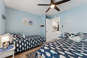 A bedroom with two beds, a ceiling fan, a nightstand, a lamp, a framed picture on the wall, and a door leading to a bathroom.