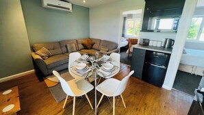 Un espacio habitable compacto con comedor, sofá, cocina y vistas al exterior.