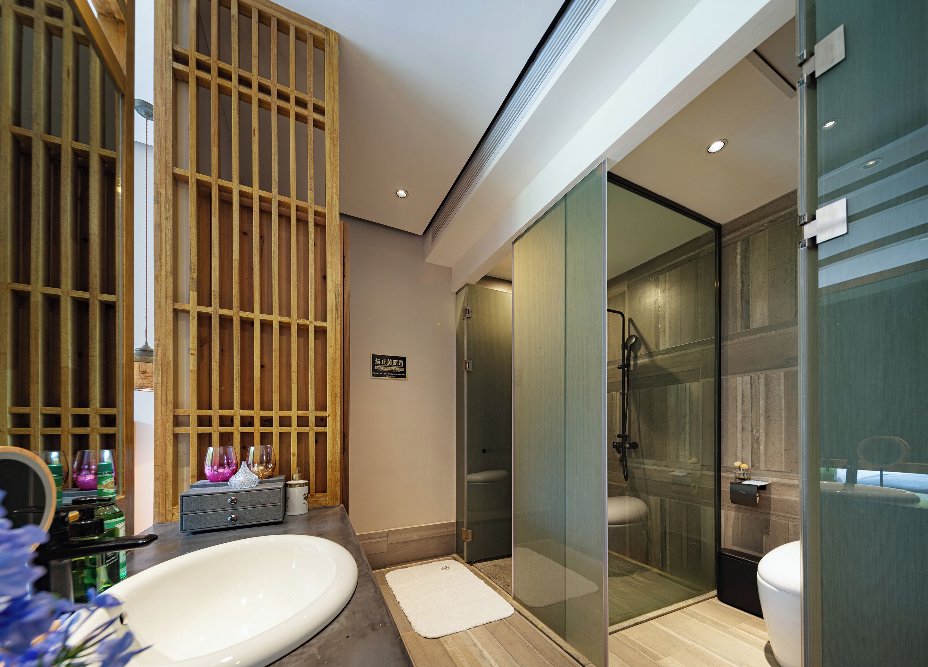 A modern bathroom with a large white sink, a glass shower enclosure, and a wooden partition.