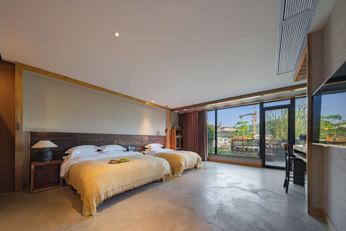 Ein modernes Hotelzimmer mit einem großen Bett, einem Nachttisch, einer Lampe und Blick ins Freie.