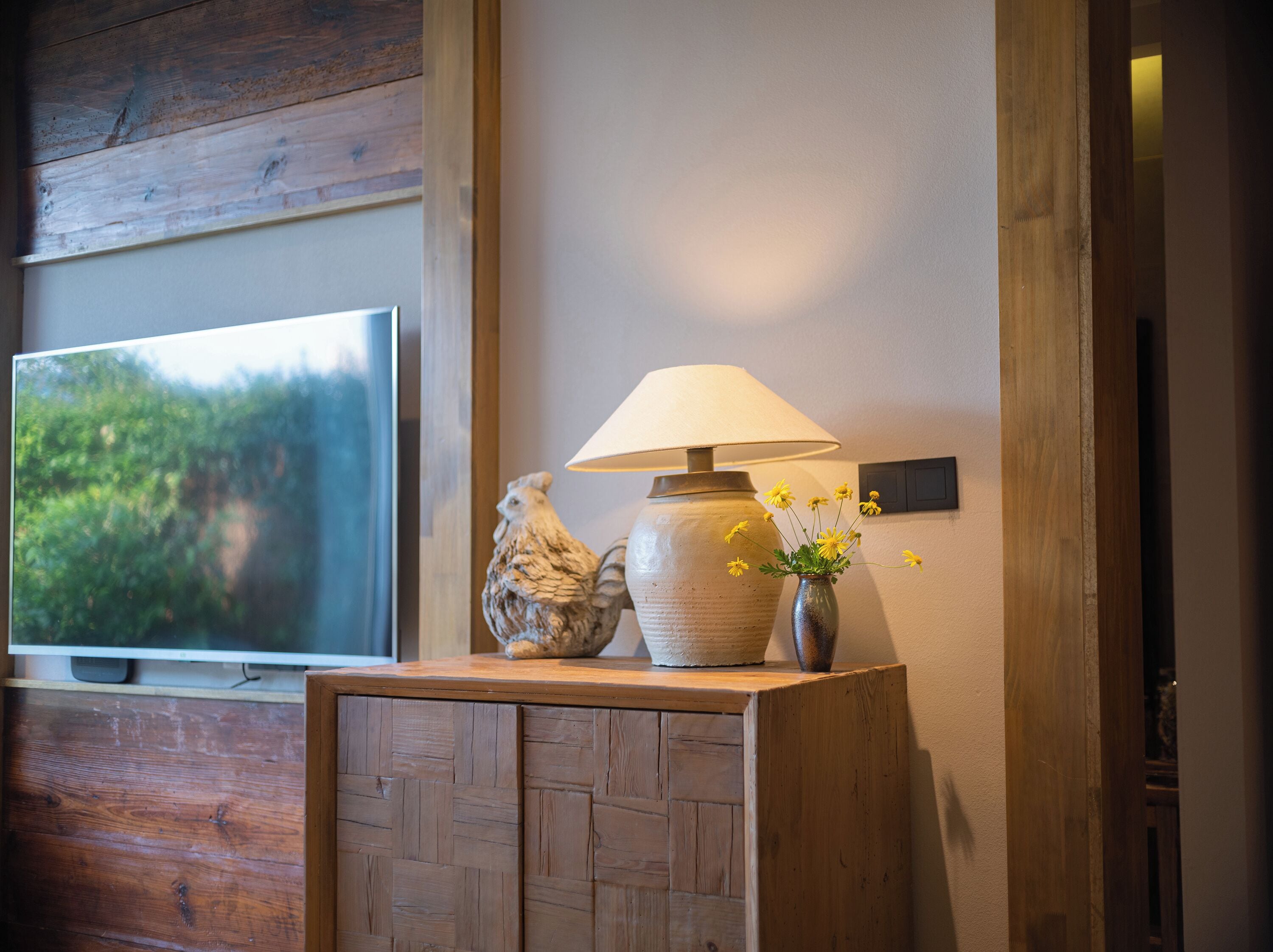 Ein Holzkabinett mit einem Fernseher darauf, einer Lampe und einer Vase mit Blumen.