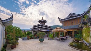 Une cour traditionnelle agrémentée d’un bâtiment de style pagode, de plantes en pot, d’un petit étang et de sièges d’extérieur.