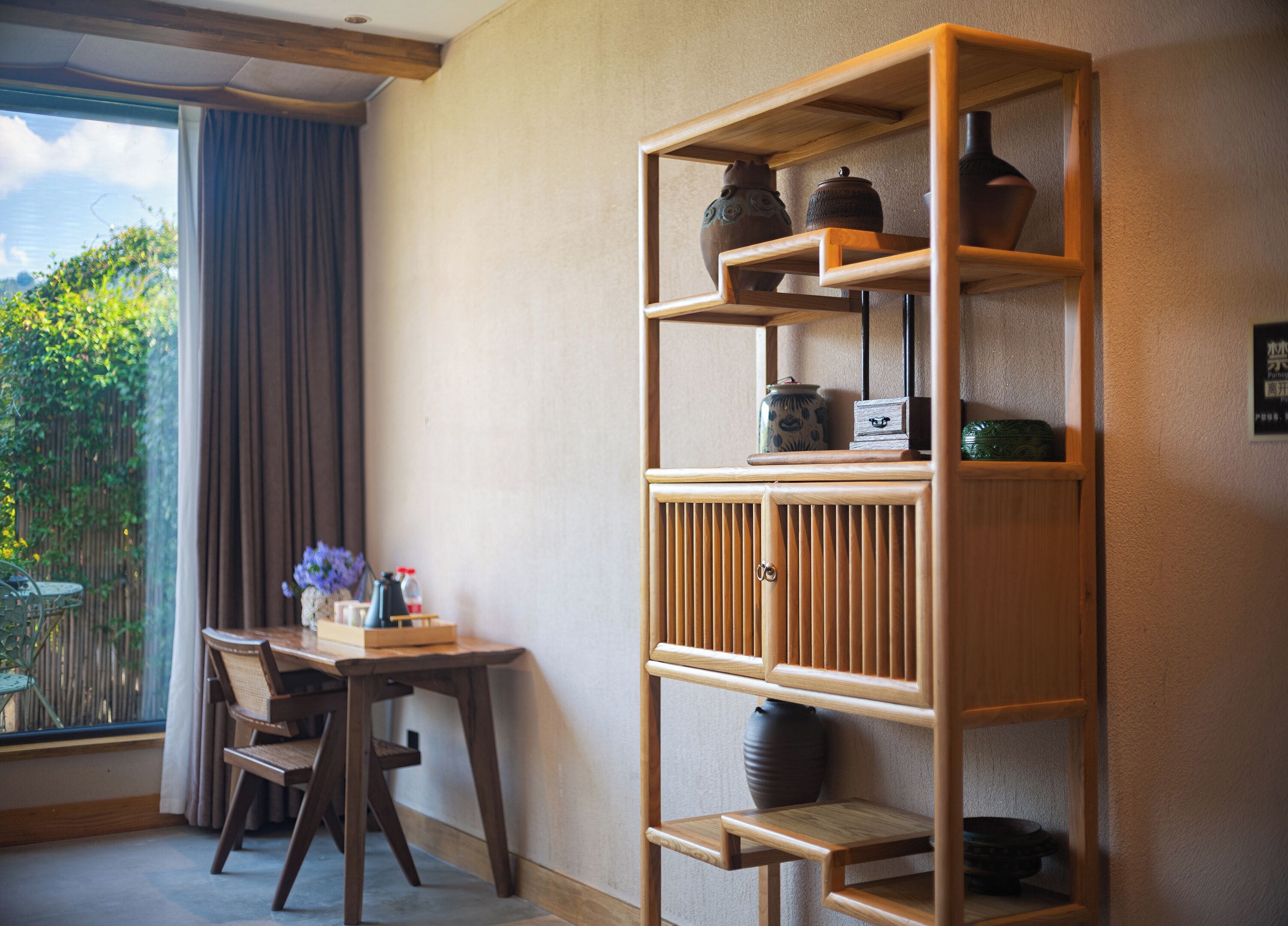 Una habitación con una estantería de madera, una mesa de comedor con sillas y vistas al exterior.