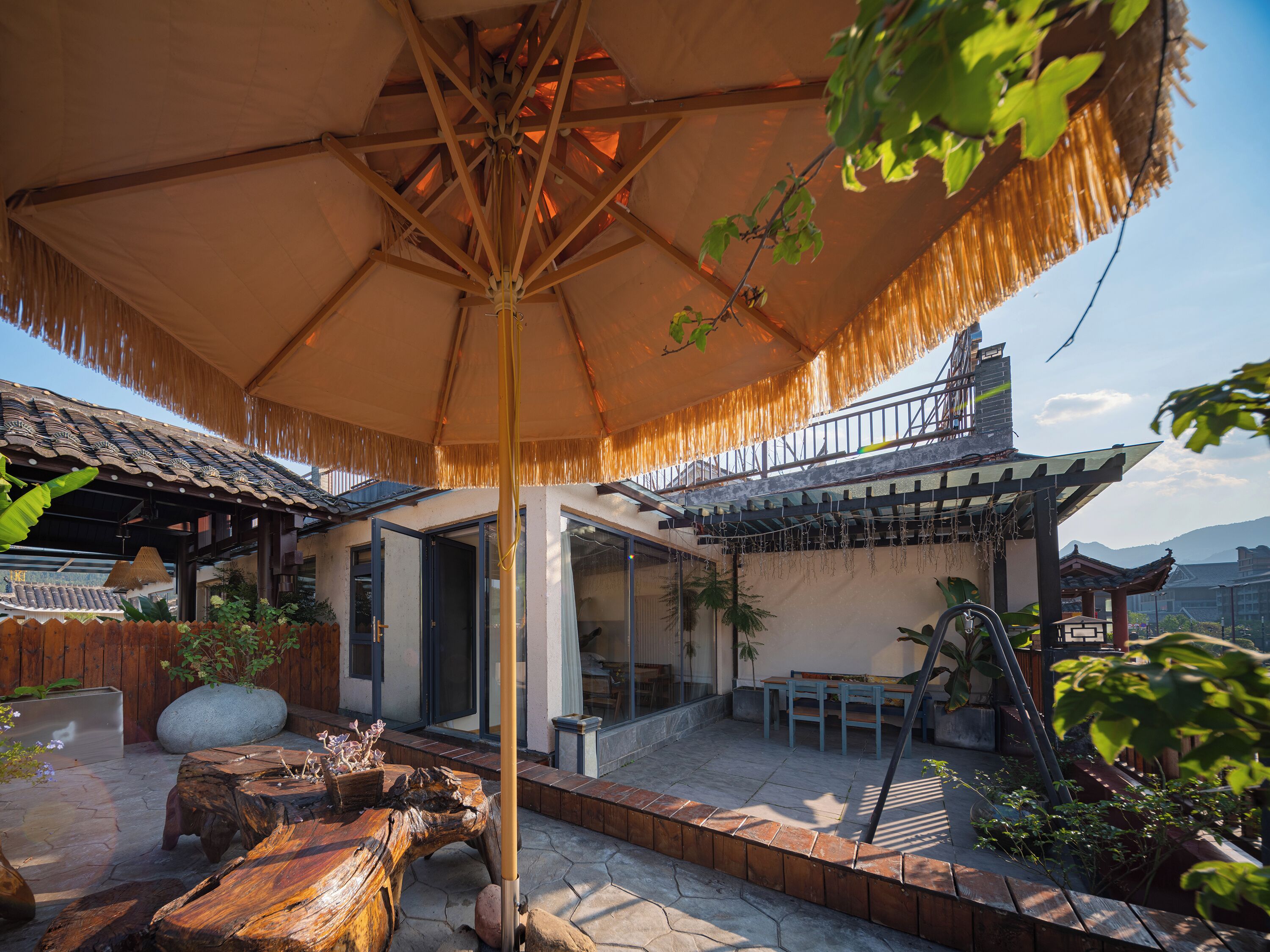 A traditional-style patio with a thatched umbrella, wooden furniture, and potted plants.