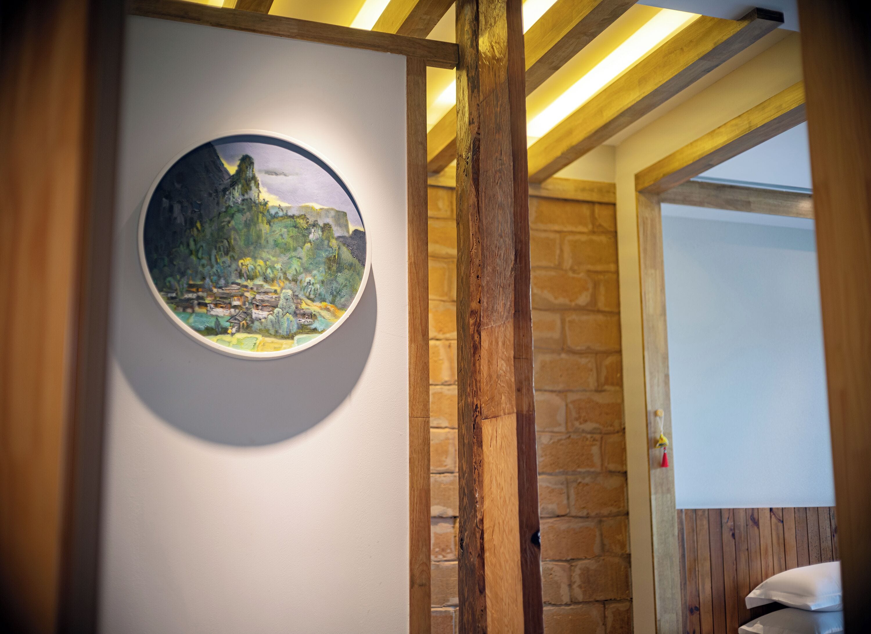 A circular painting of a landscape on a wall, a wooden beam, and a stone wall.