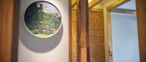 A circular painting of a landscape on a wall, a wooden beam, and a stone wall.