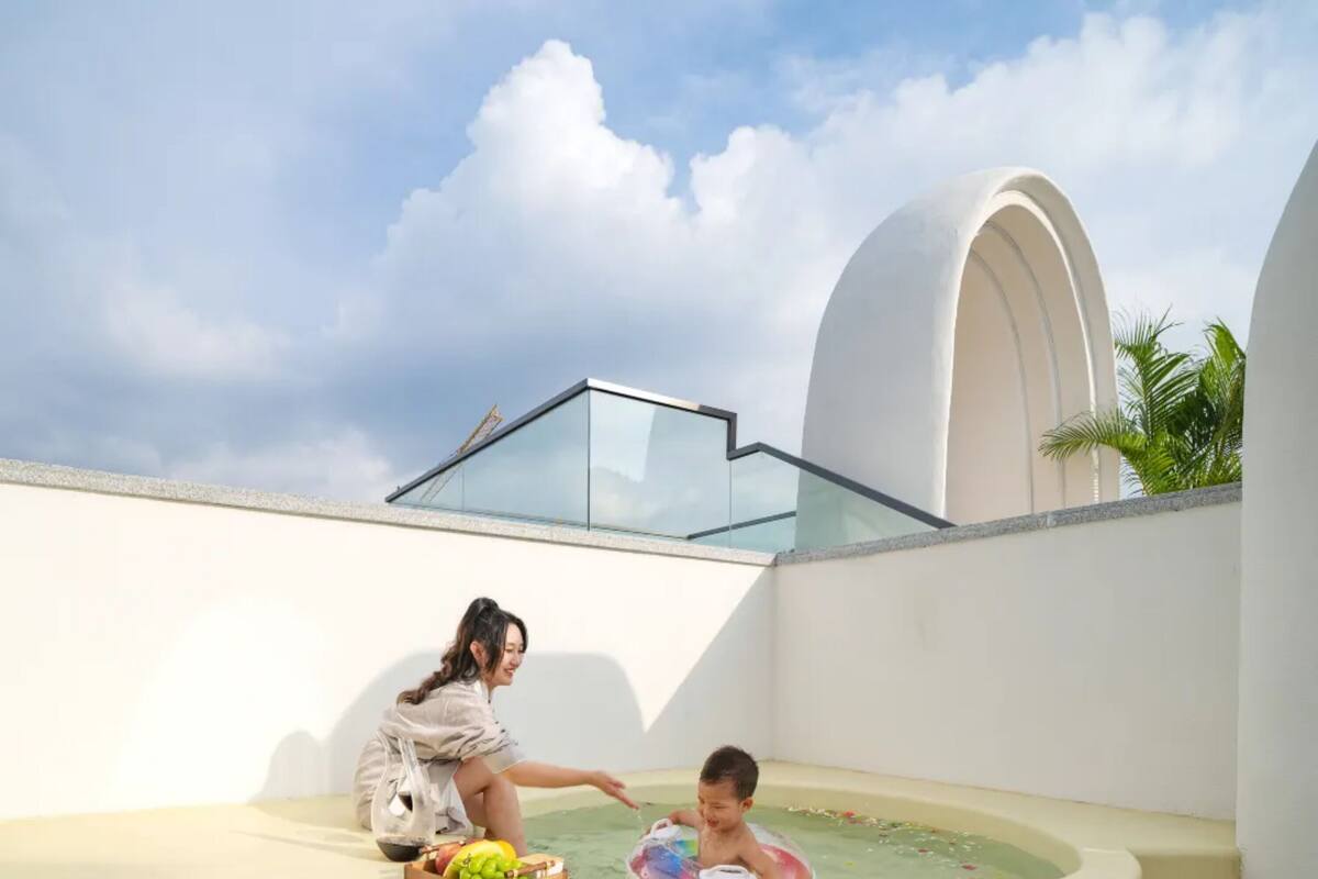 Ein Poolbereich auf dem Dach mit Glasbrüstung, ein Kind spielt im Wasser und eine Frau sitzt in der Nähe.