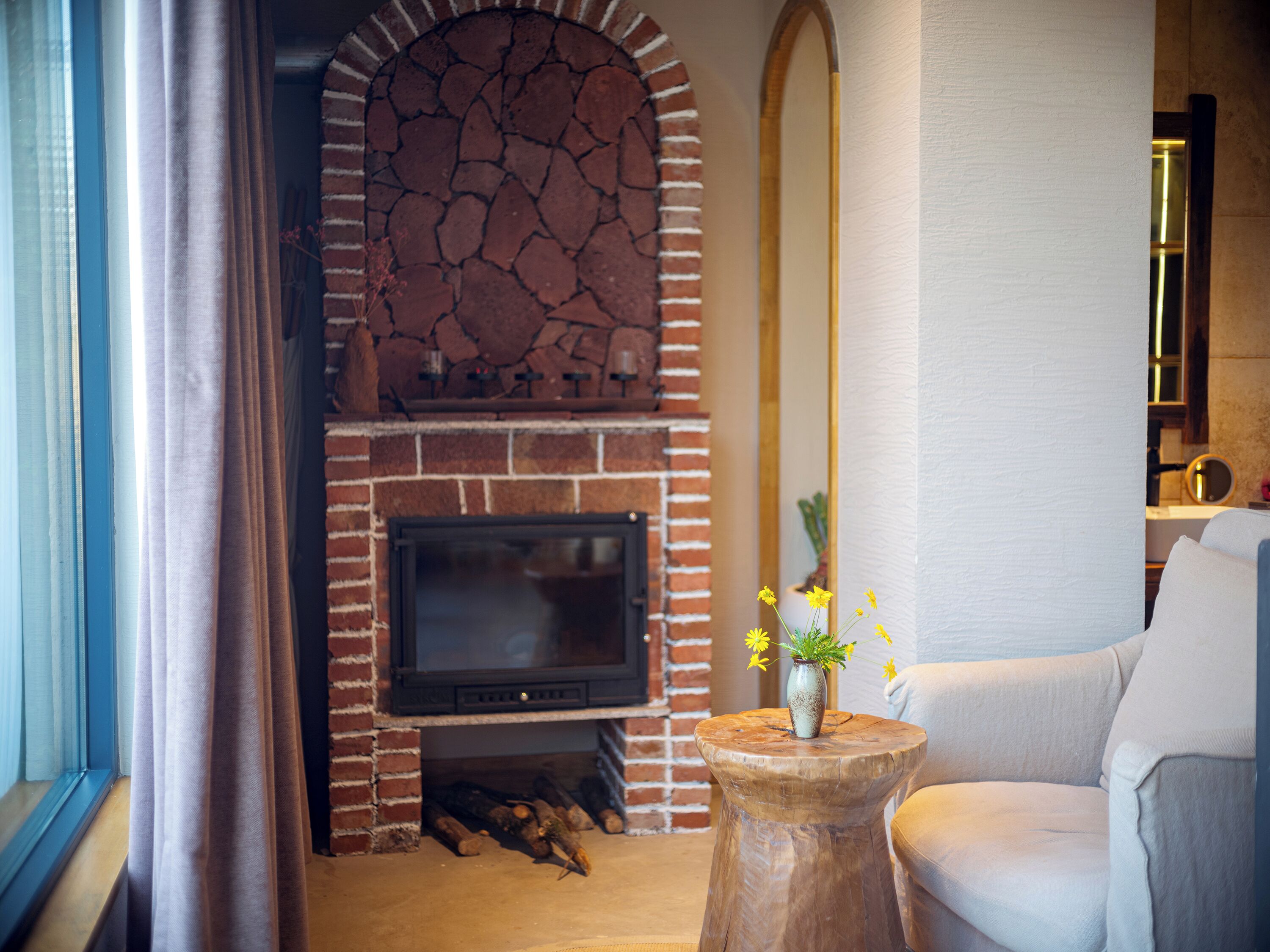 Una sala de estar con chimenea de ladrillo, un televisor y una mesita de madera con flores.