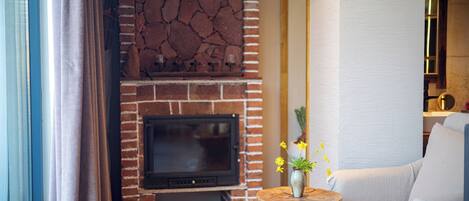 A living room with a brick fireplace, a television, and a wooden side table with flowers.