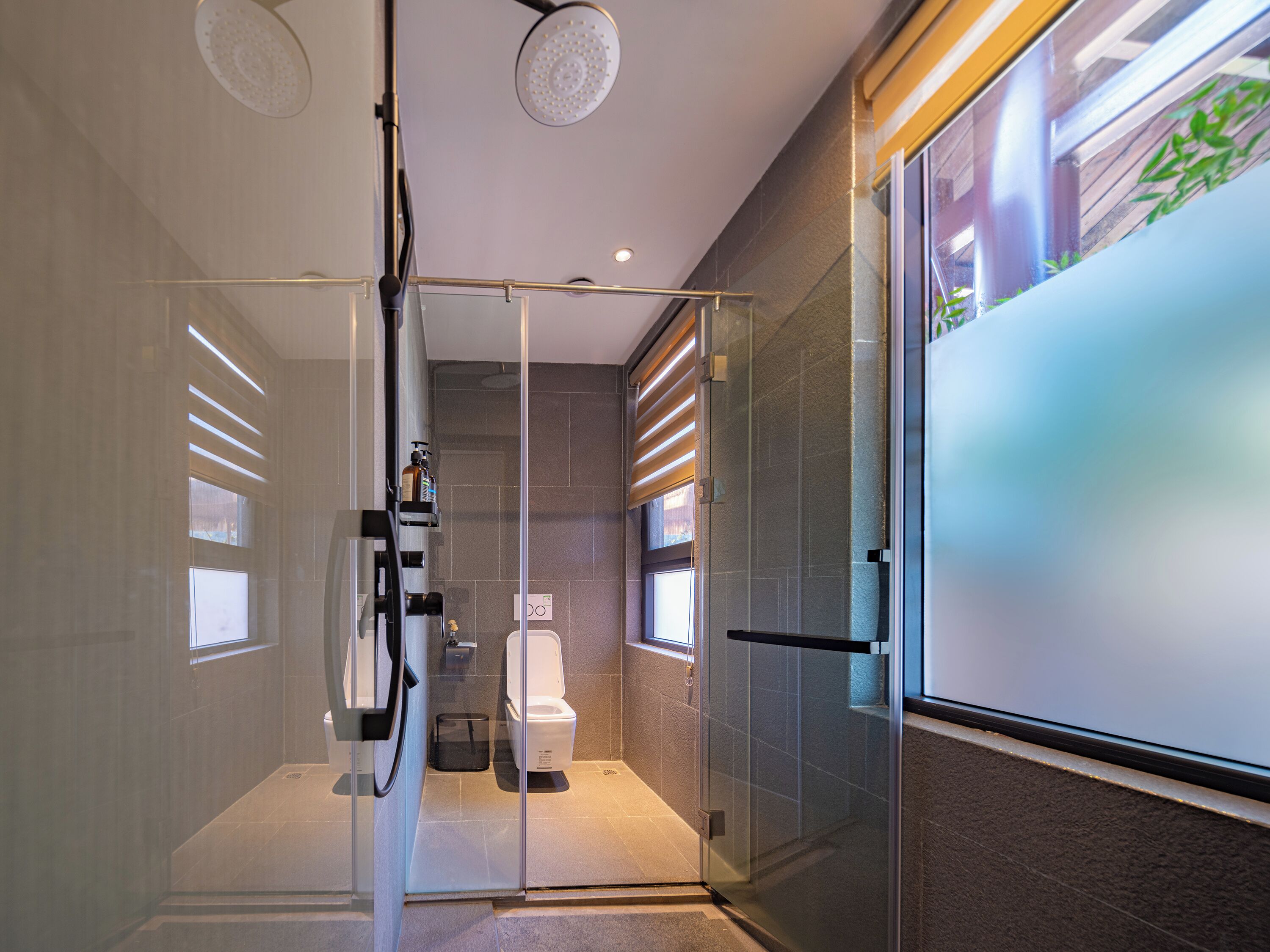A modern bathroom with a glass shower enclosure, a toilet, and a large window.