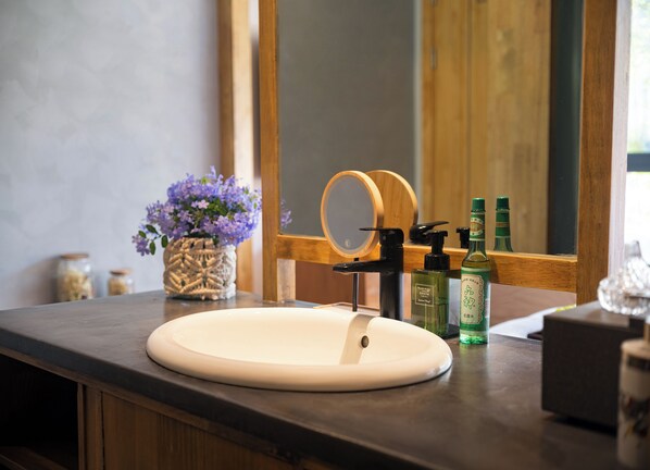 A bathroom with a round sink, a wooden-framed mirror, and a vase with purple flowers. - Wang Yun Residence Boutique Homestay (Zhangjiajie)