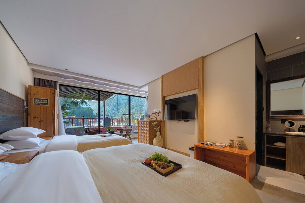 Ein Hotelzimmer mit zwei Betten, einem Fernseher, einem Schreibtisch mit einer Vase und Blick auf einen Berg.