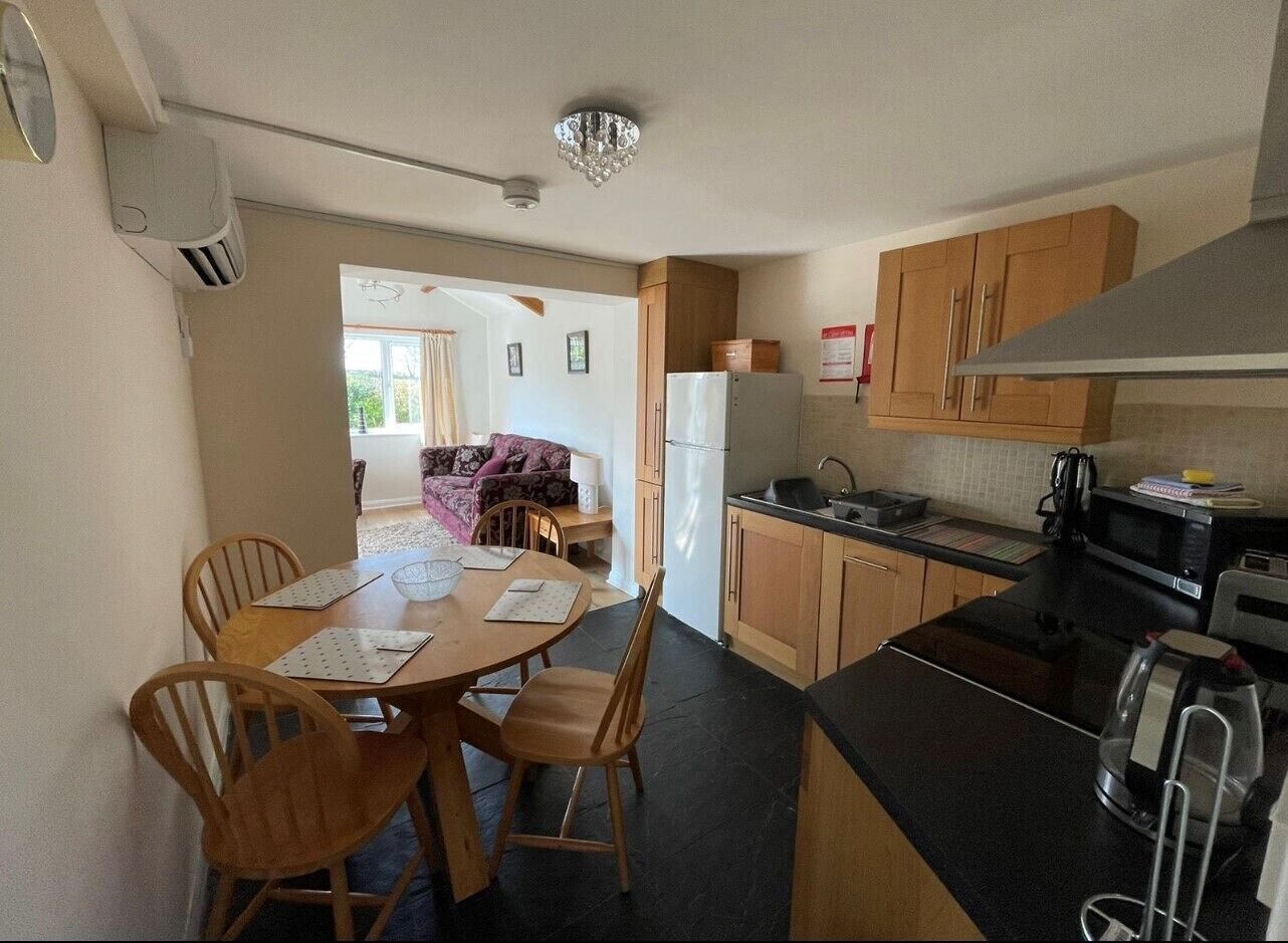 A compact kitchen with wooden cabinets, a dining table with chairs, and a refrigerator.